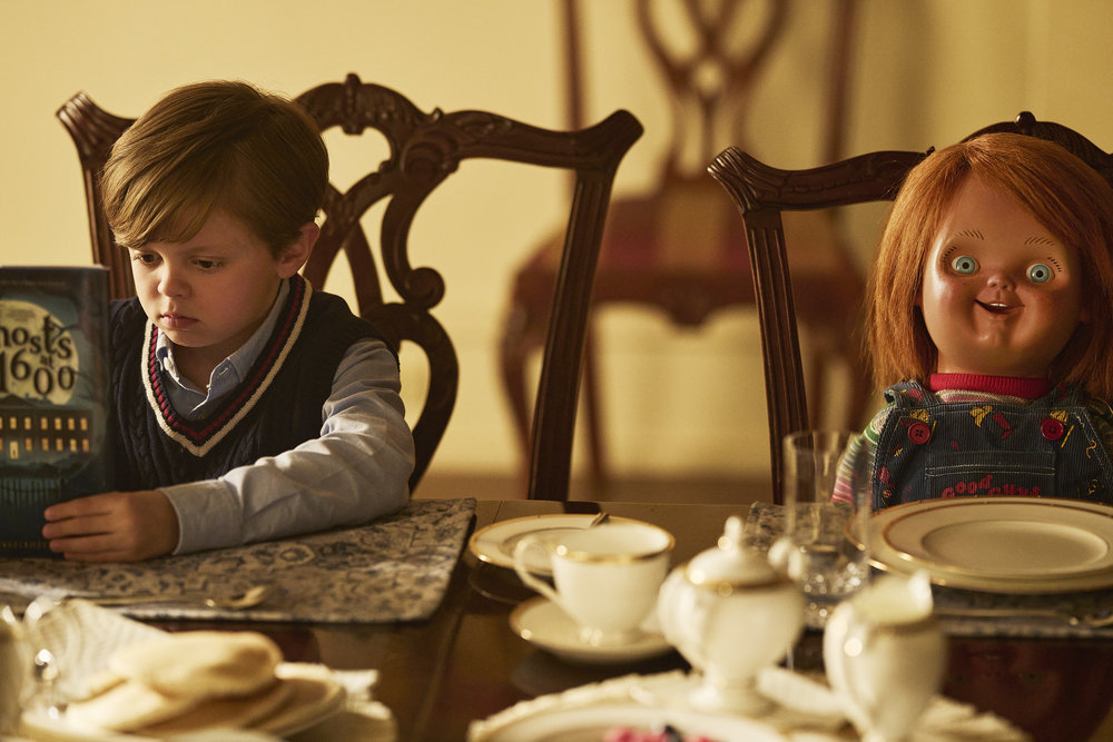 kid and chucky doll sitting a dining table