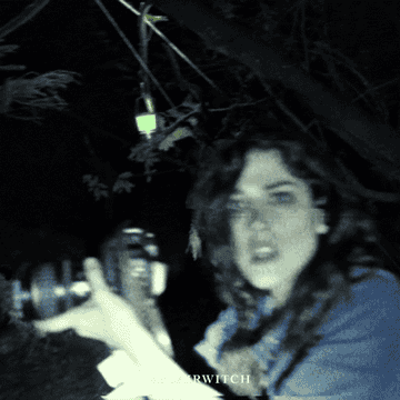 a young woman holds a camera in shaky digital footage in the woods