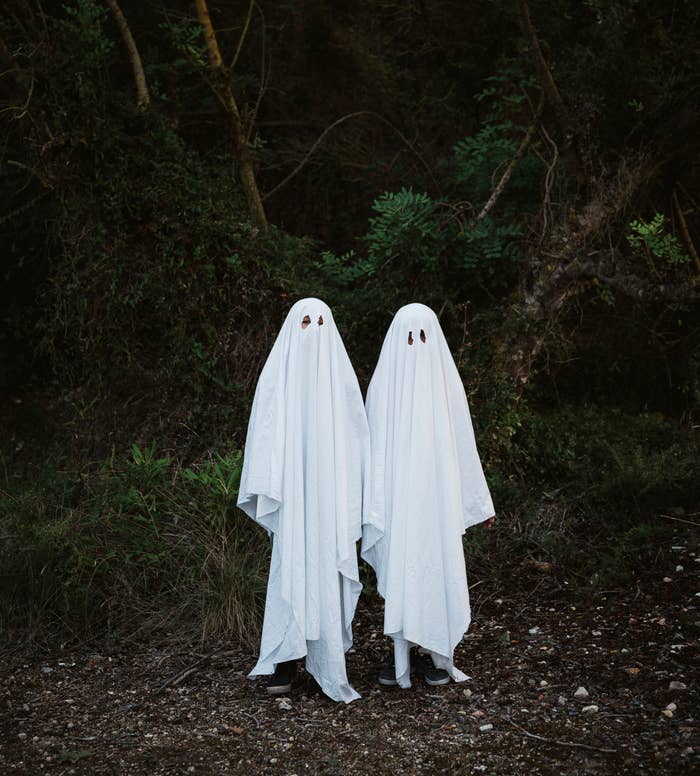two children dressed as ghosts in sheets stand in the woods