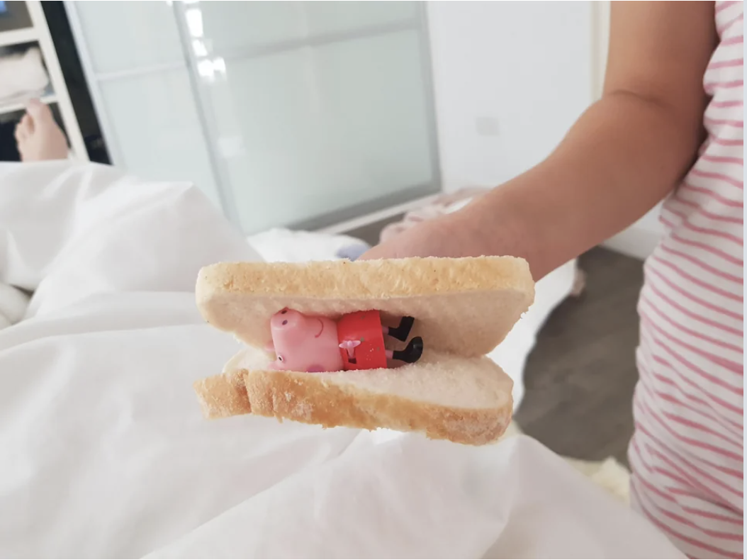 A kid holding two slices of bread with a toy pig between them