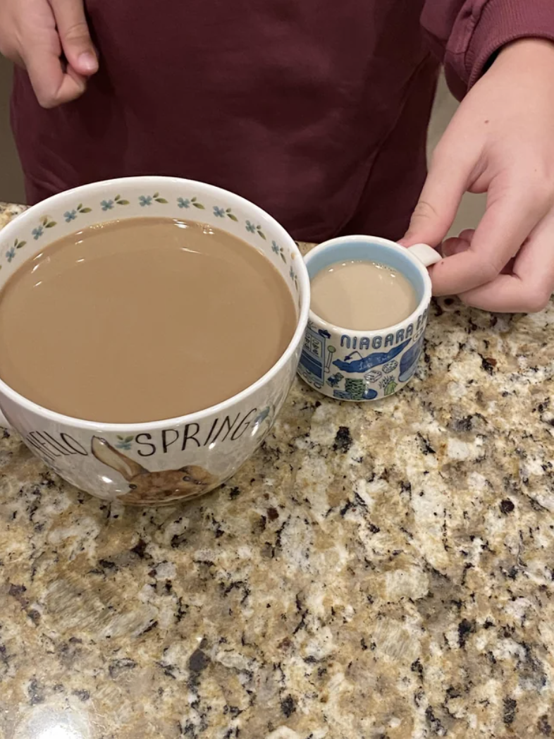 A tiny mug of very light coffee next to a larger mug of darker coffee