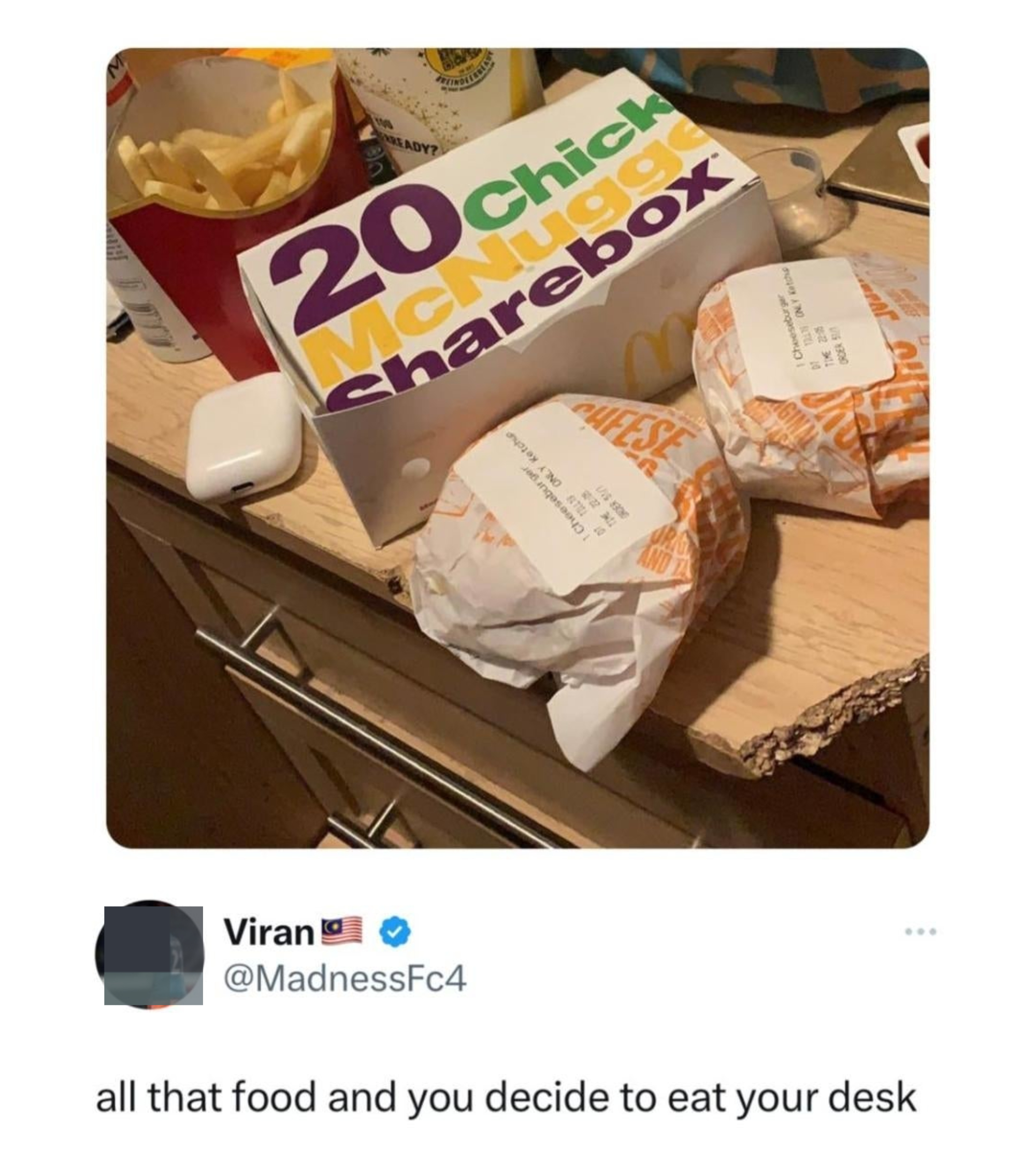 Lots of takeout fast food on a desk, which has a chunk missing from the side of the top, with comment, "all that food and you decide to eat your desk"