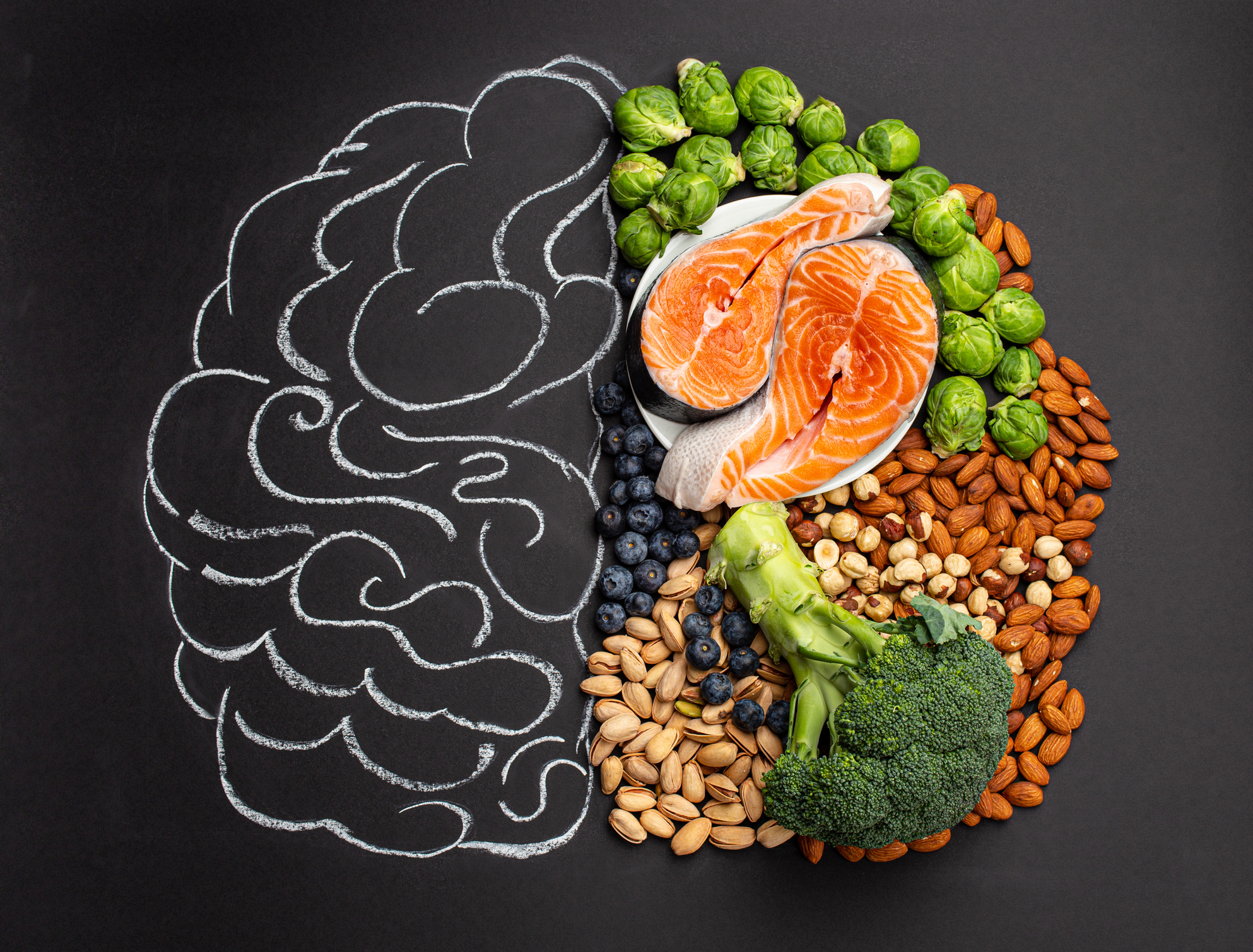 Chalk hand drawn brain with assorted food that is good for brain health and memory: fresh salmon fish, green vegetables, nuts, and berries