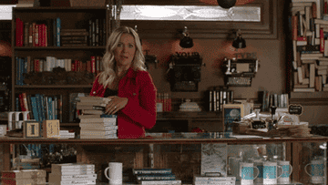 A woman running a bookstore and waving at a customer