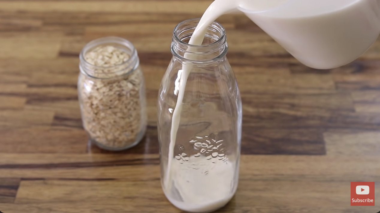 person pouring oat milk into a glass bottle
