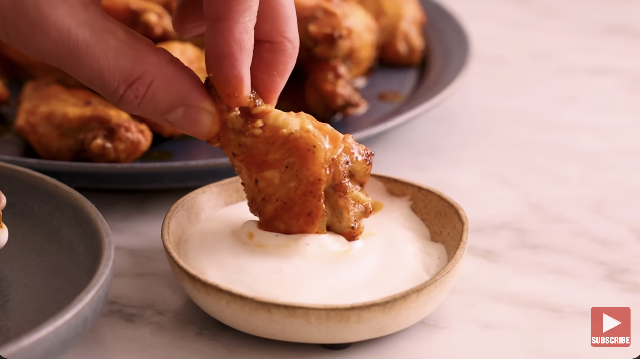 hand dipping chicken wing in ranch dressing