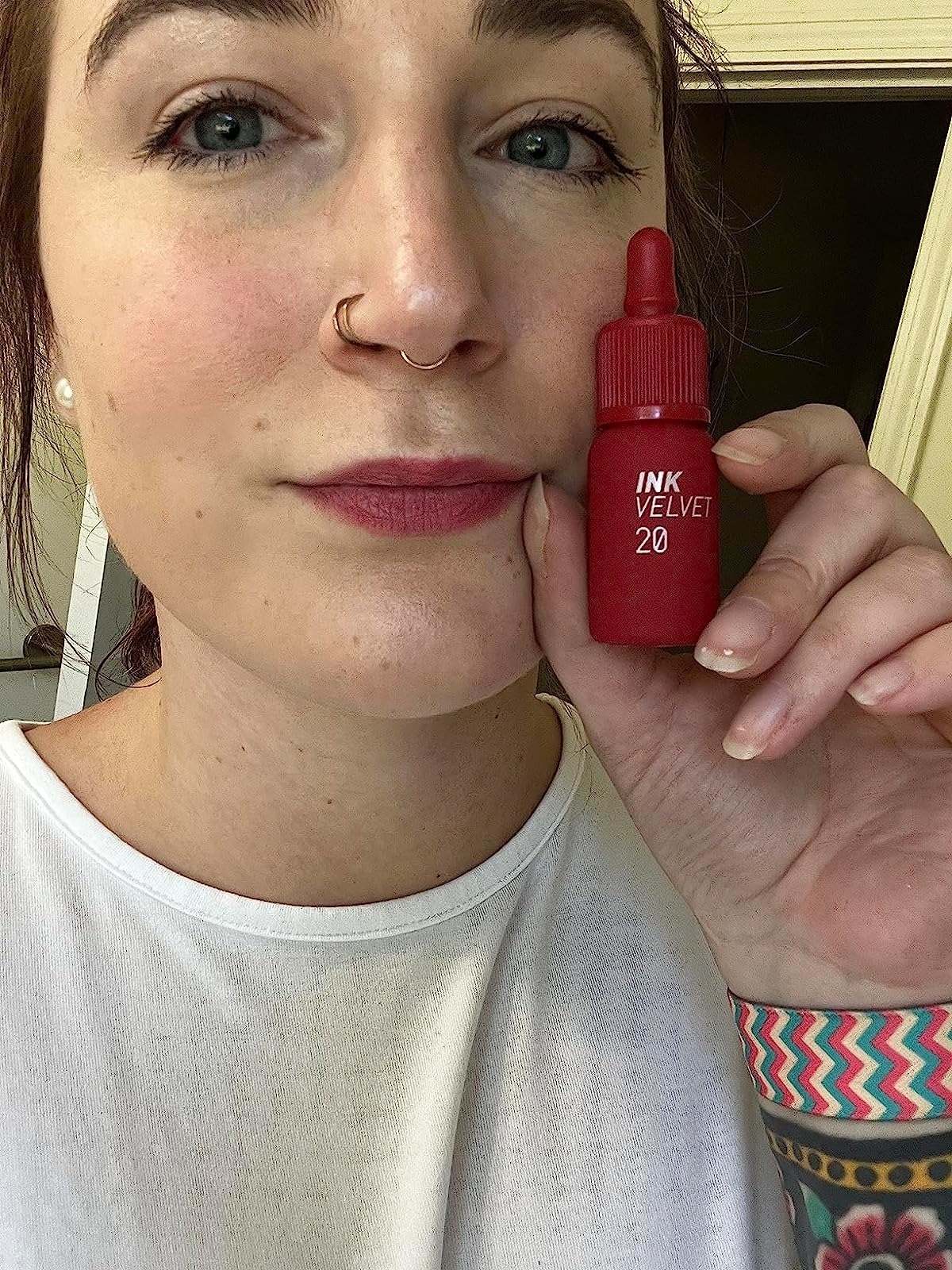 a reviewer holding the bottle next to their tinted red lips