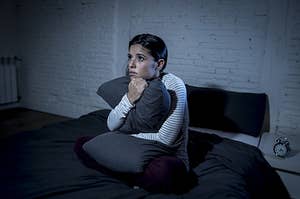 A woman on her bed clutching a pillow and looking scared