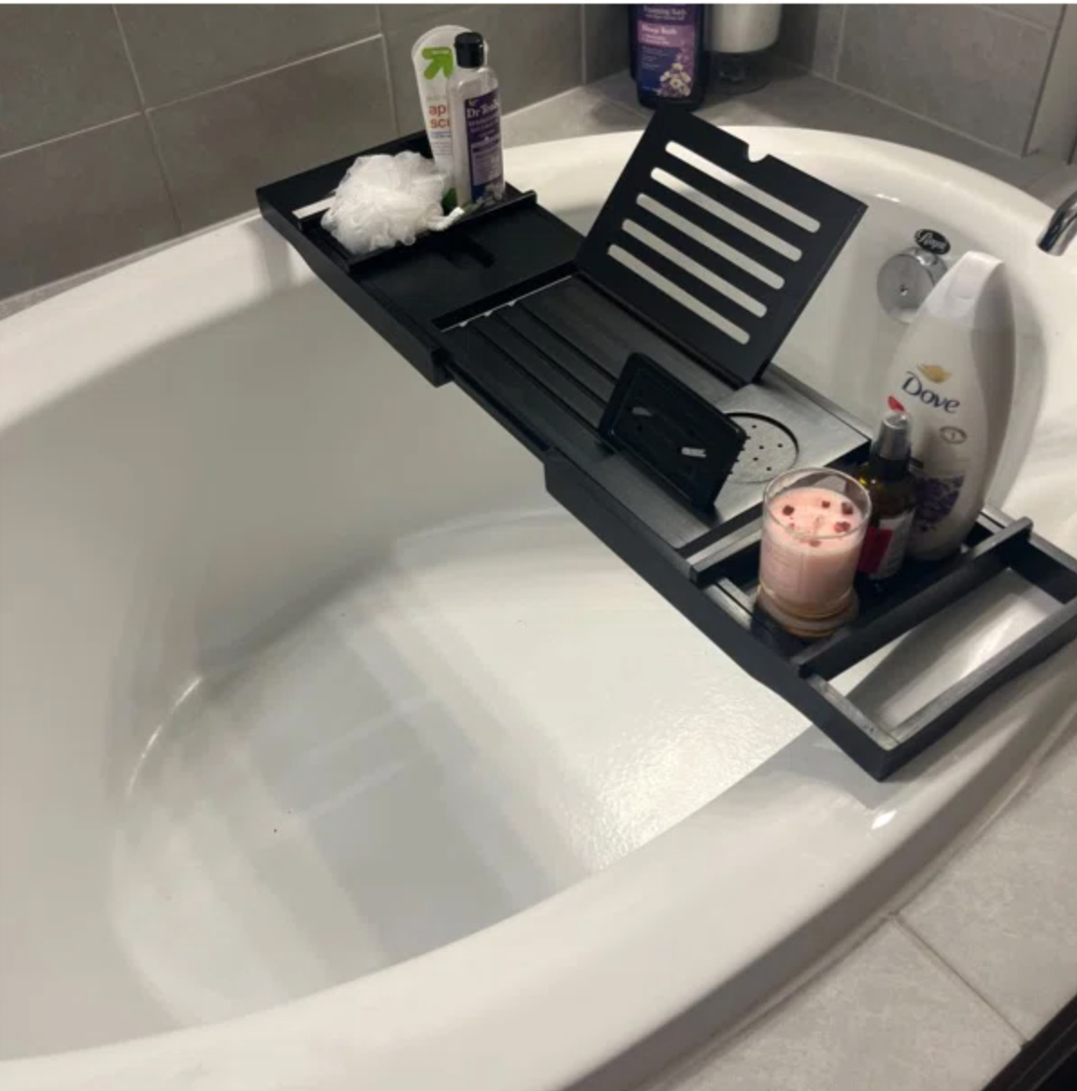 a black bath tub caddy holding shampoo bottles, a phone and a drink