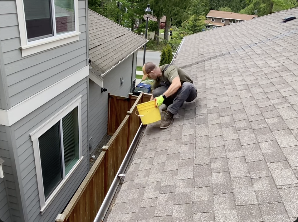 man cleaning the gutters on the roof of a house