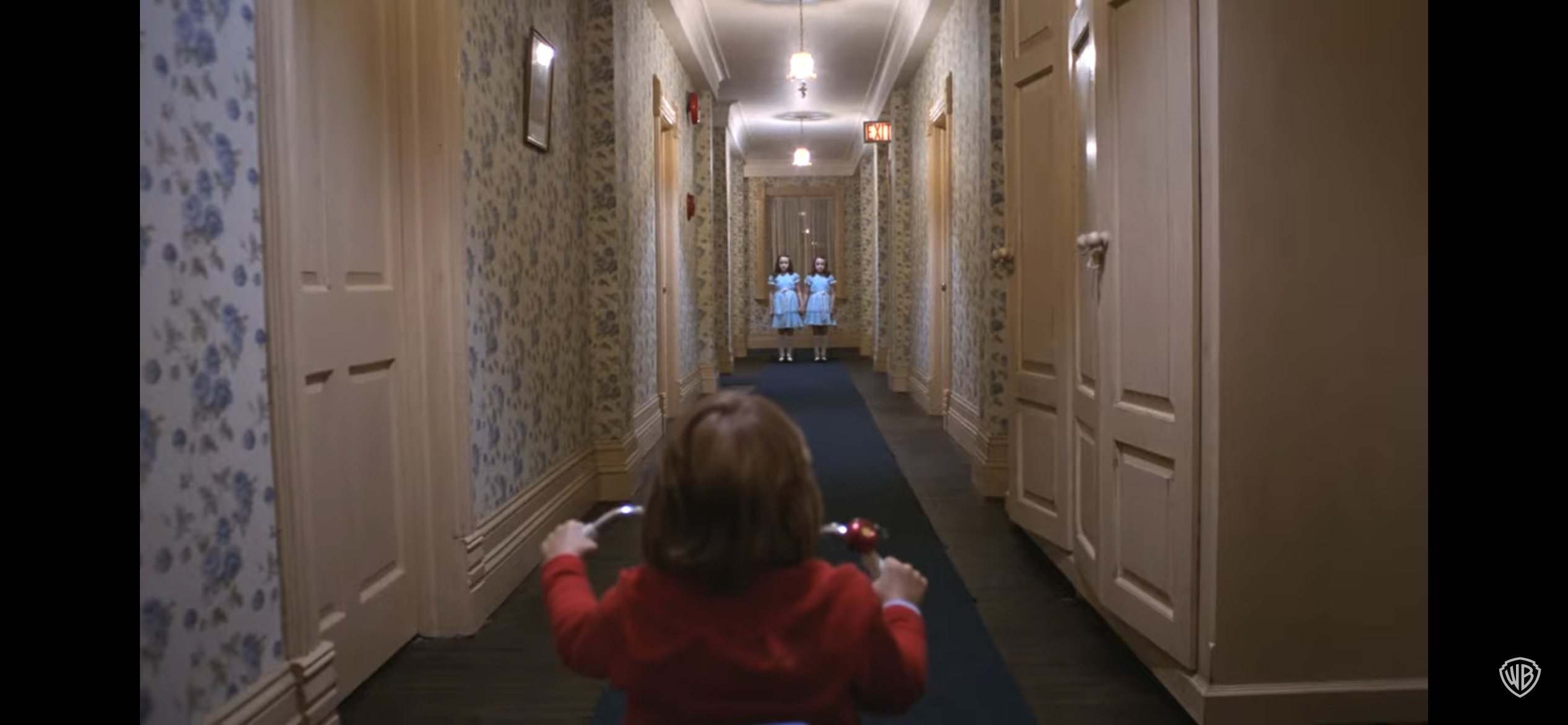 Kid riding tricycle in eerie hallway with two twin girls at end of the hall