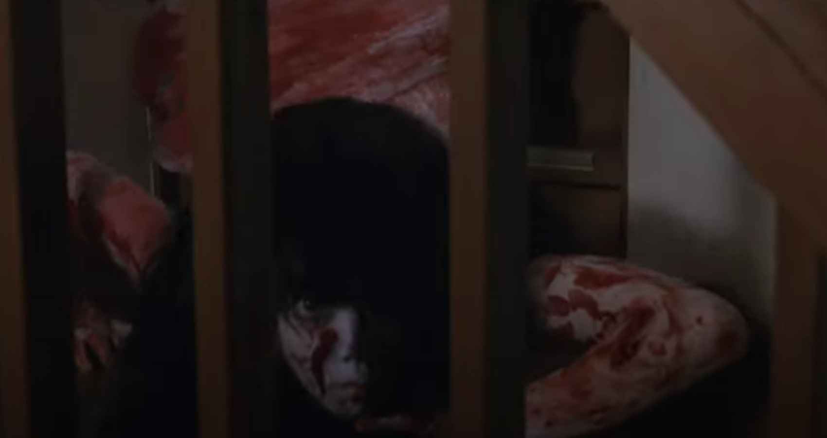 A spooky kid covered in blood and looking through bars