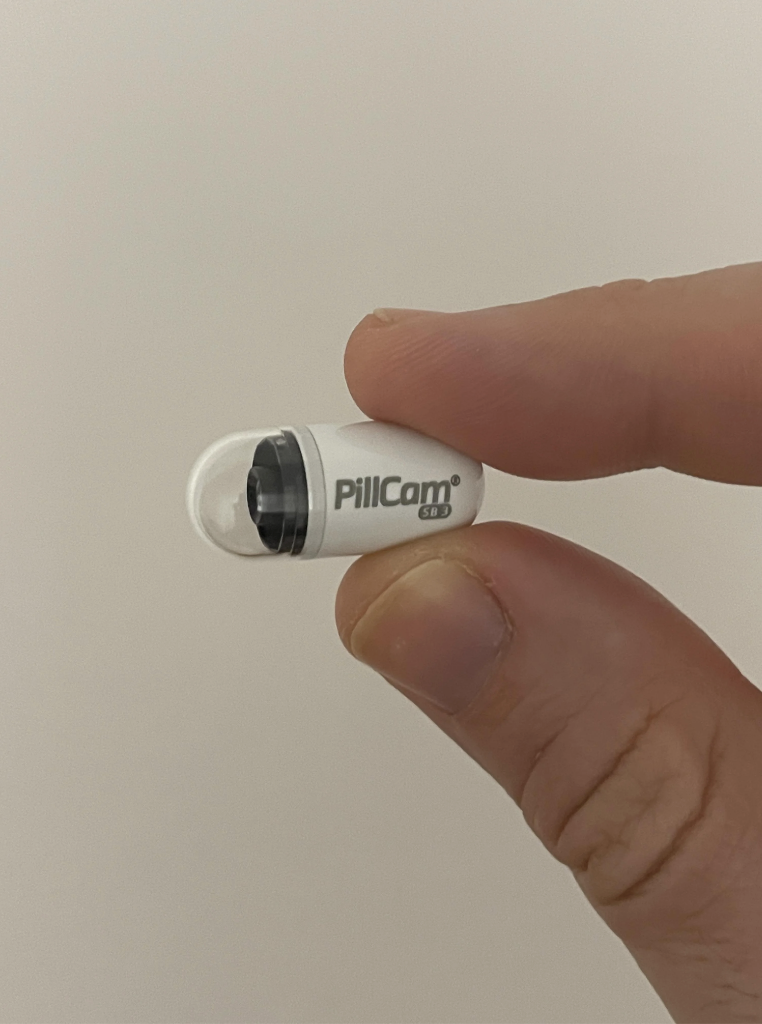 A hand holding a PillCam capsule