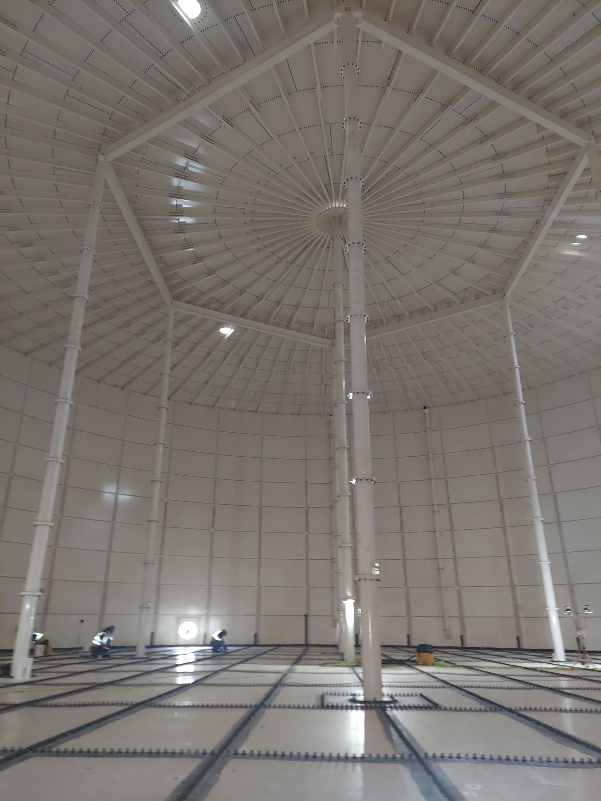 An enormous, cavernous empty room with a checkered floor, long poles, and spoked roof