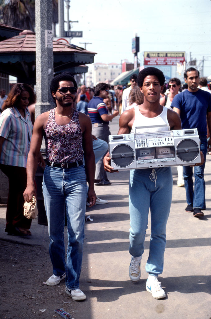 Two men are walking down the street holding a boom box