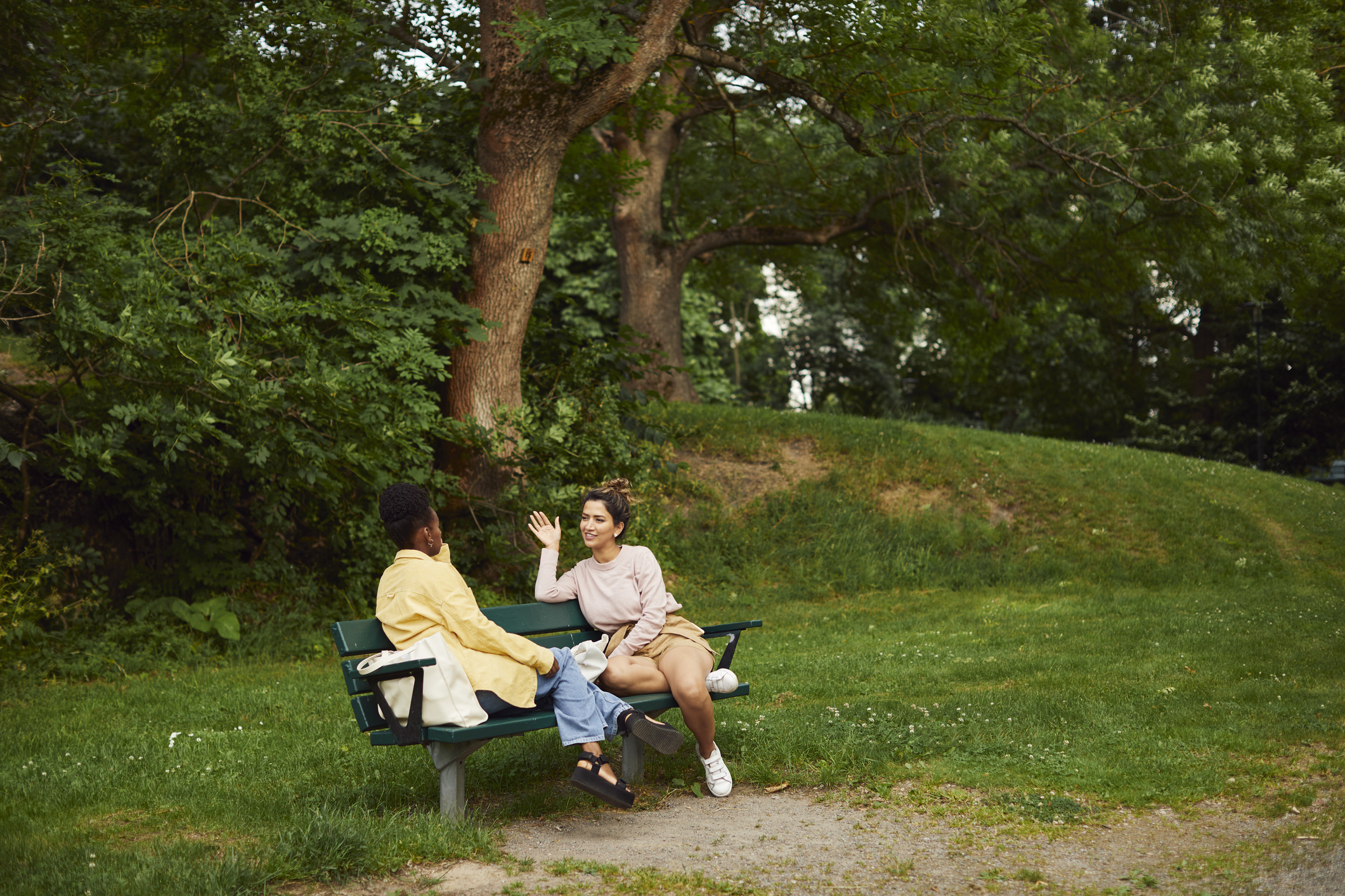 Two friends are sitting on a park bench, talking