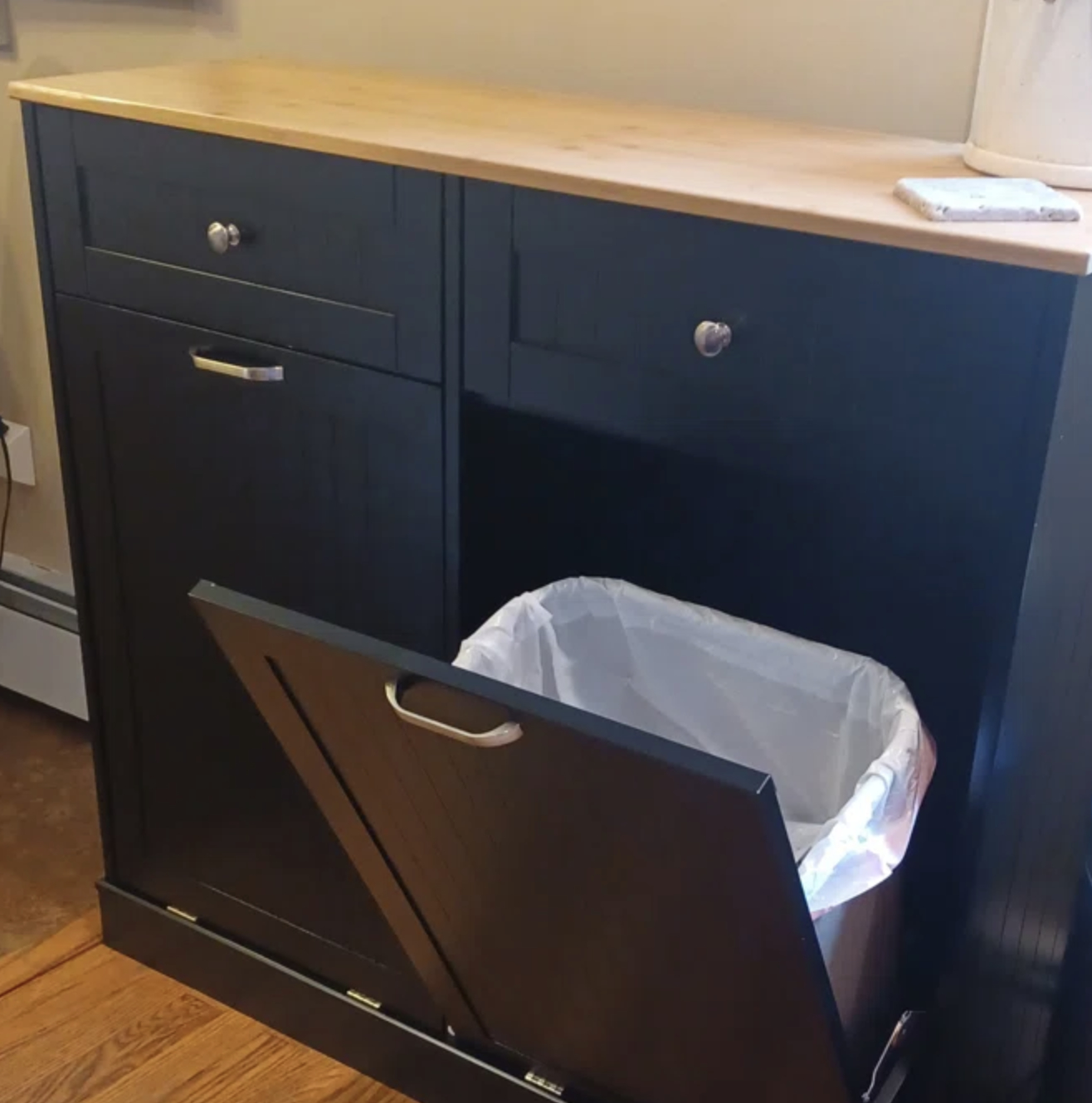 a wooden cabinet with trash can tilting out