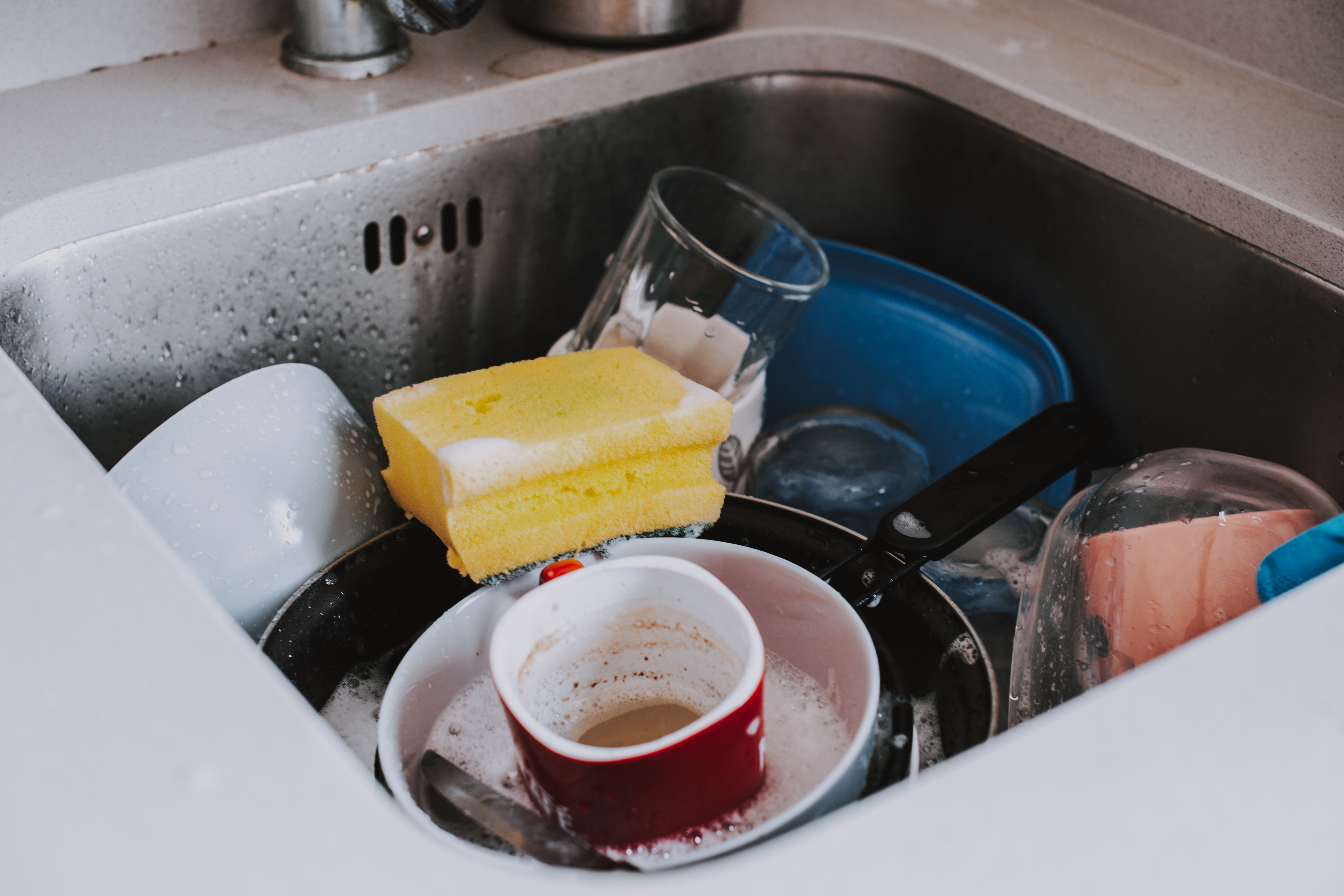 A sponge sitting atop dirty dishes in a kitchen sink