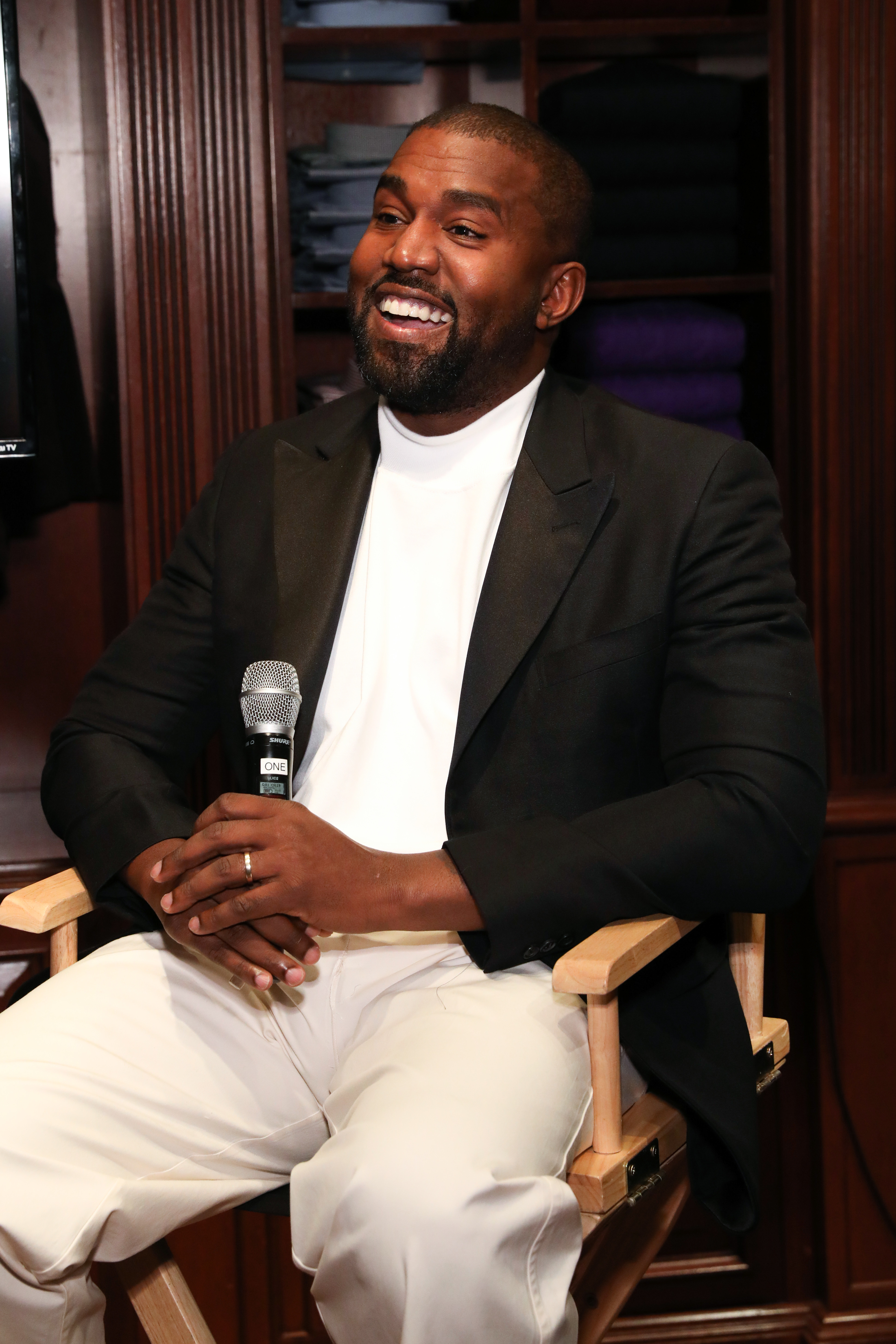 Closeup of Kanye West smiling as he sits and holds a microphone
