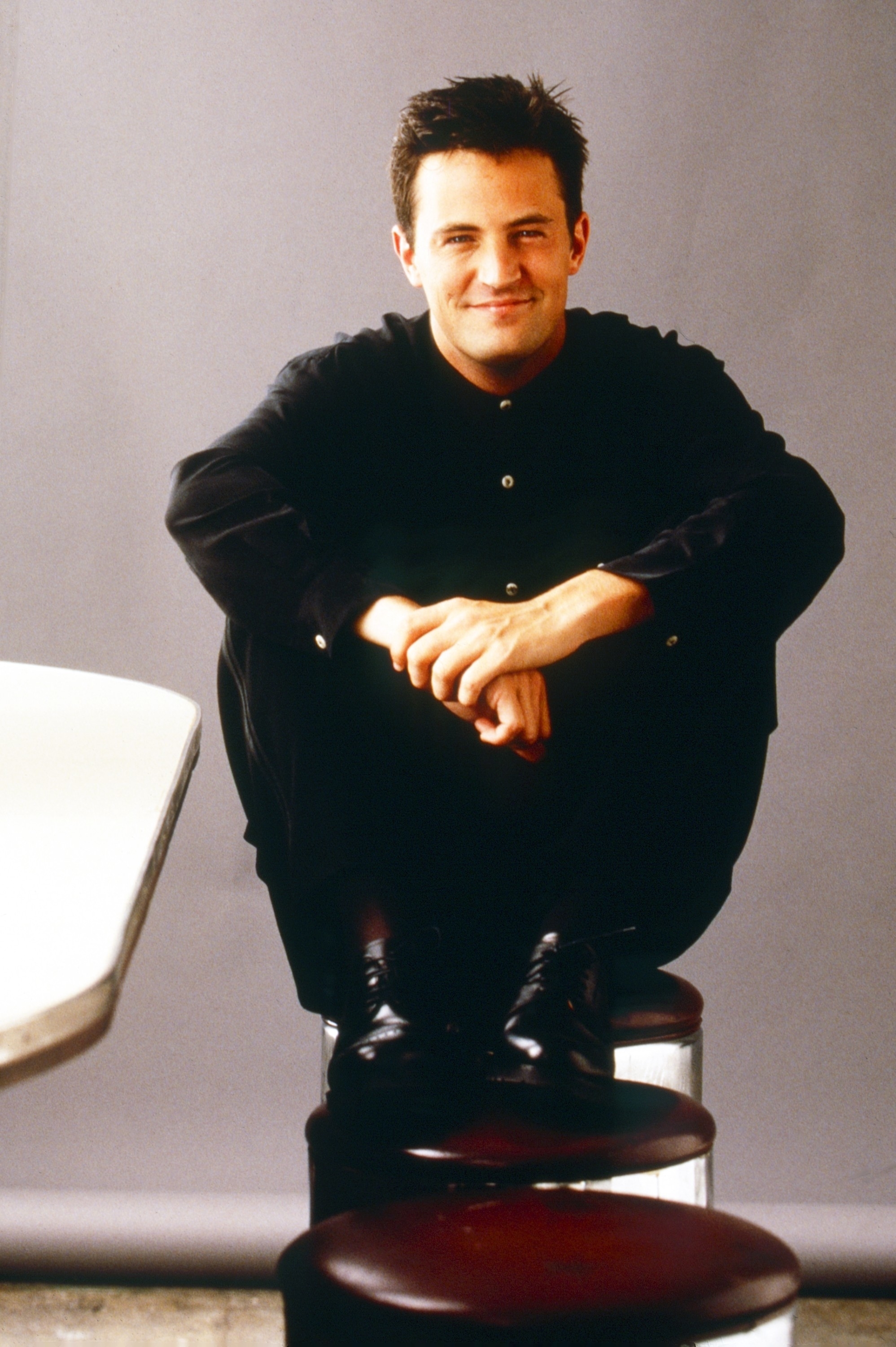 Closeup of Matthew Perry sitting on a stool in a promo shot