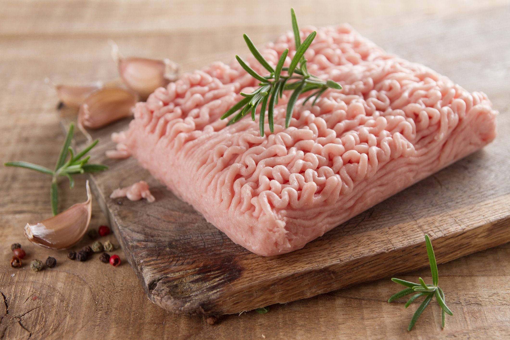 Raw ground turkey on a cutting board with a sprig of rosemary on top