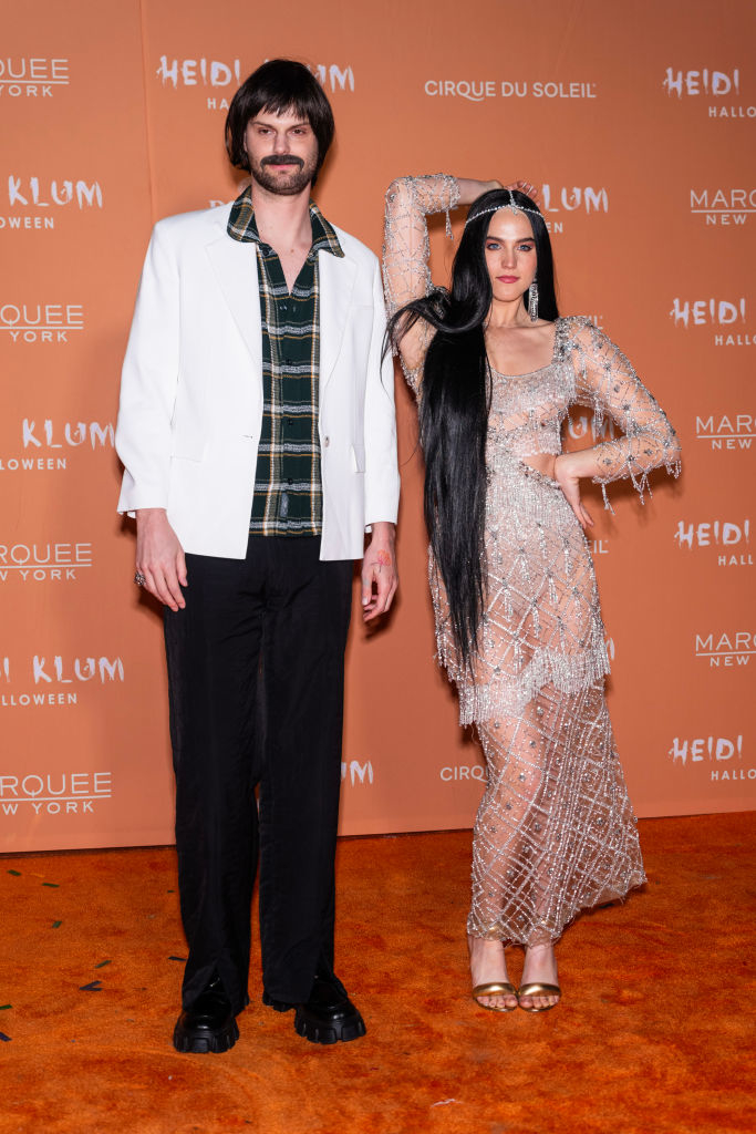 both wearing wigs, him in an old-fashioned suit and her in a bedazzled dress