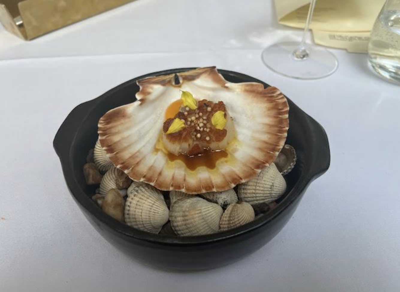 A scallop is served on top of a big seashell, which is served on a bed of other shells