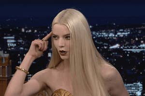 anya taylor-joy holds a finger to her forehead as if to say, "think"