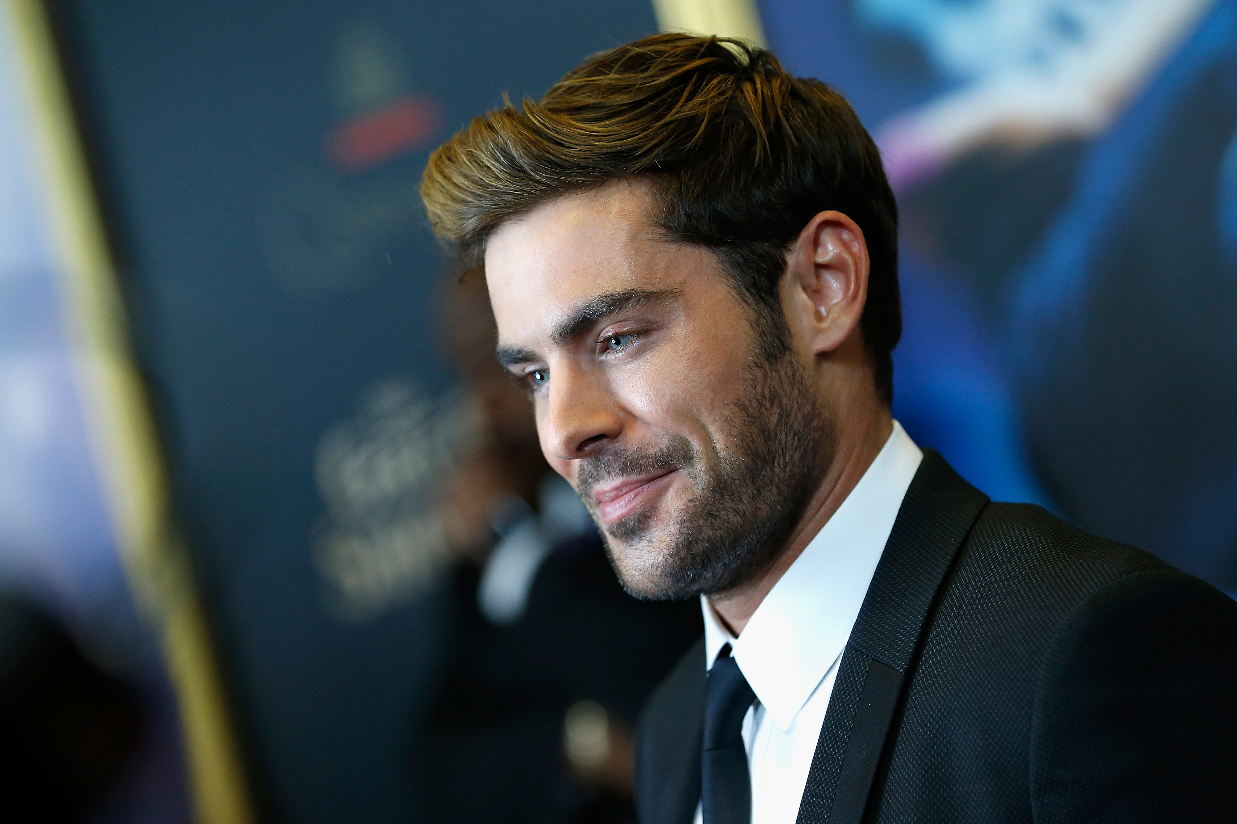 Close-up of Zac smiling in a suit and tie at a media event