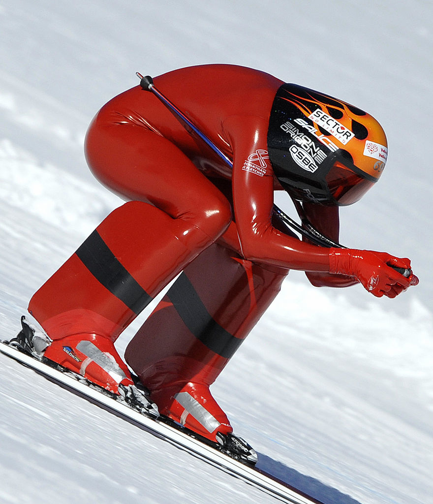 A person crouched over skis going downhill and wearing a latex-looking red outfit
