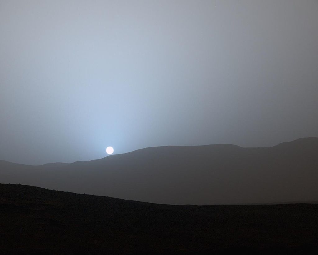 A misty, foggy view of the sun just visible over a slightly hilly landscape