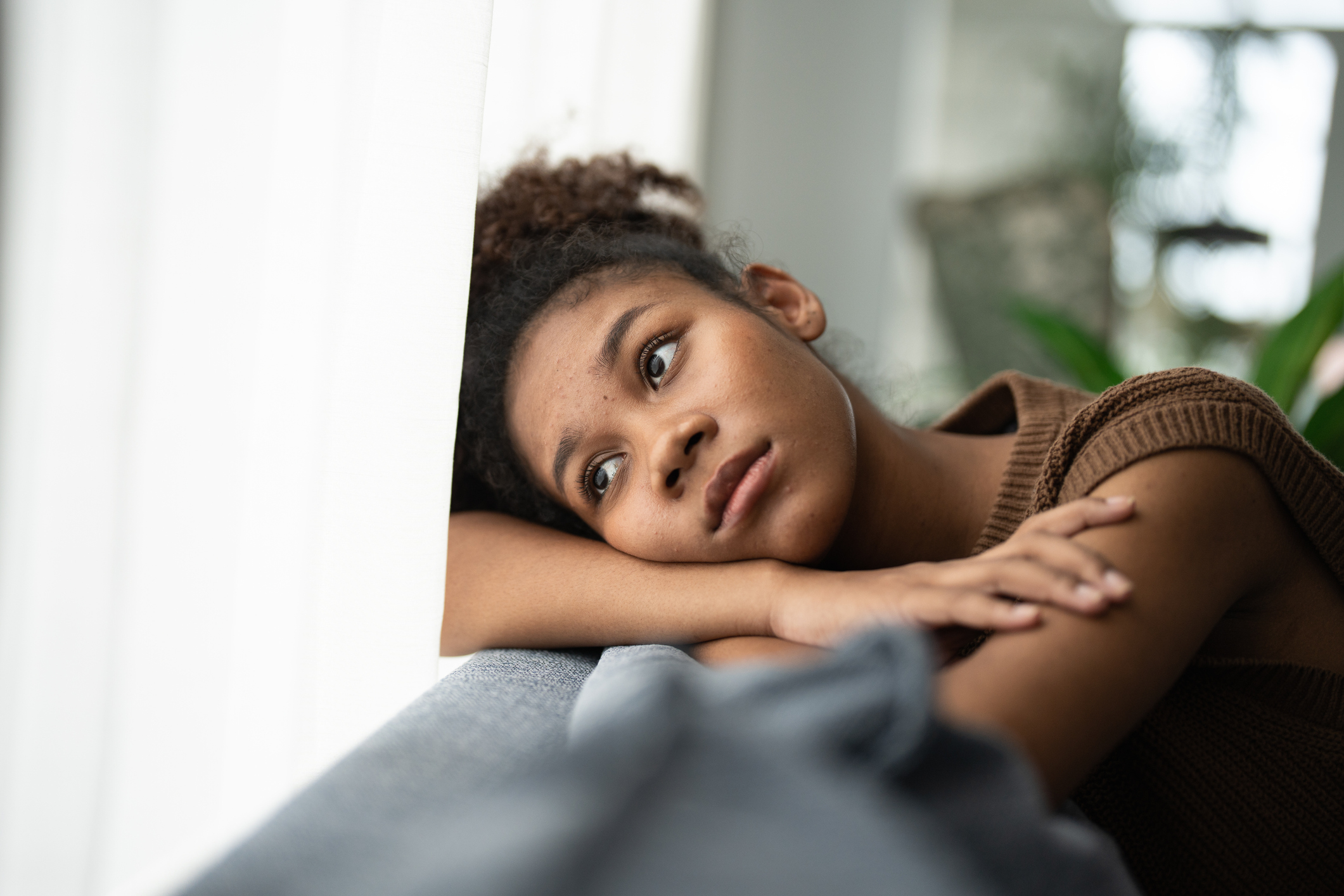a young black woman sitting on her couch looking out of a window