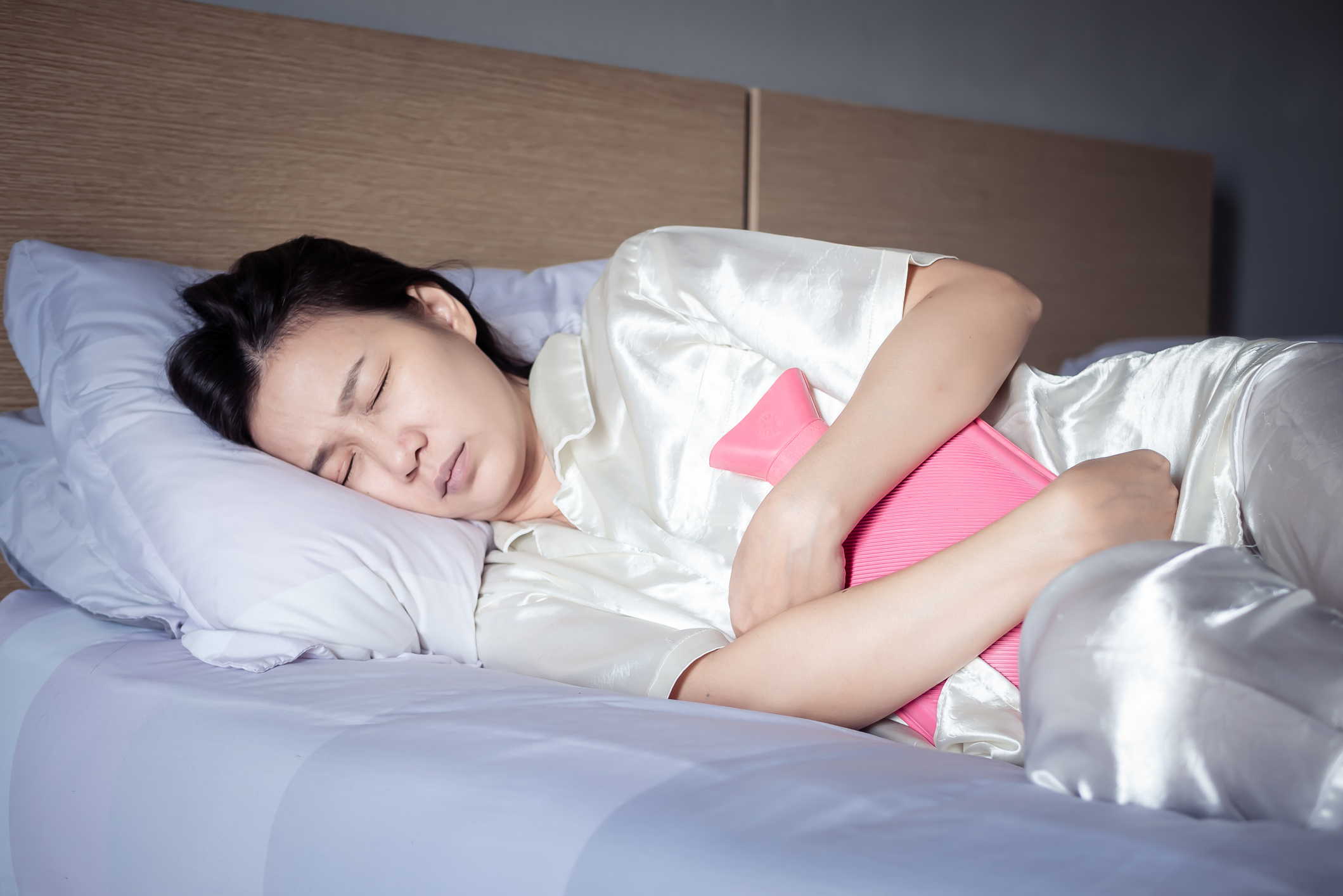 an asian woman lying in bed holding a hot water bottle