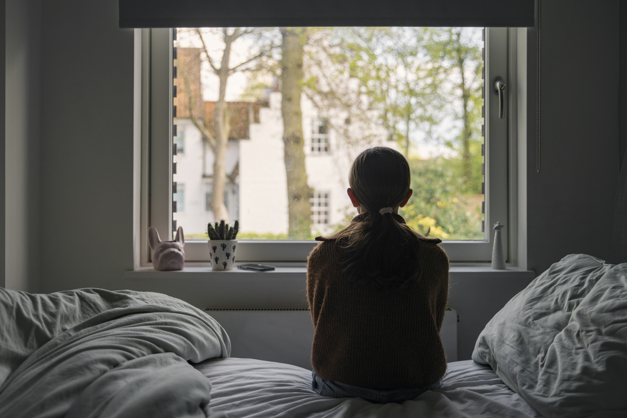 a young girl sitting on her bed and looking out of a window