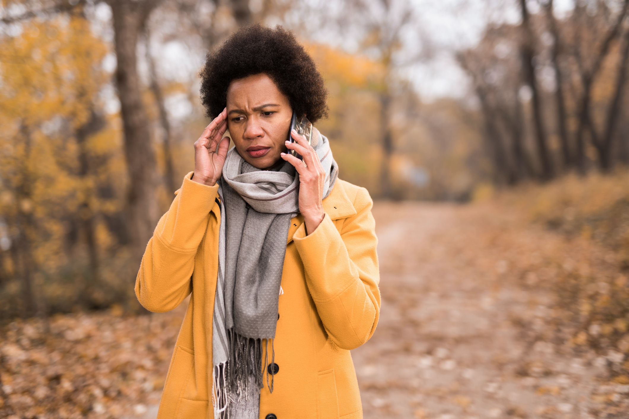 a black woman looking concerned while on the phone walking through a park