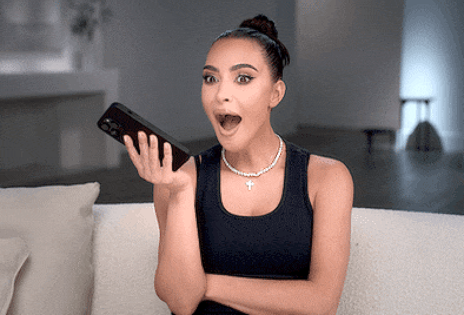 Kim K holding a phone with her mouth open in shock