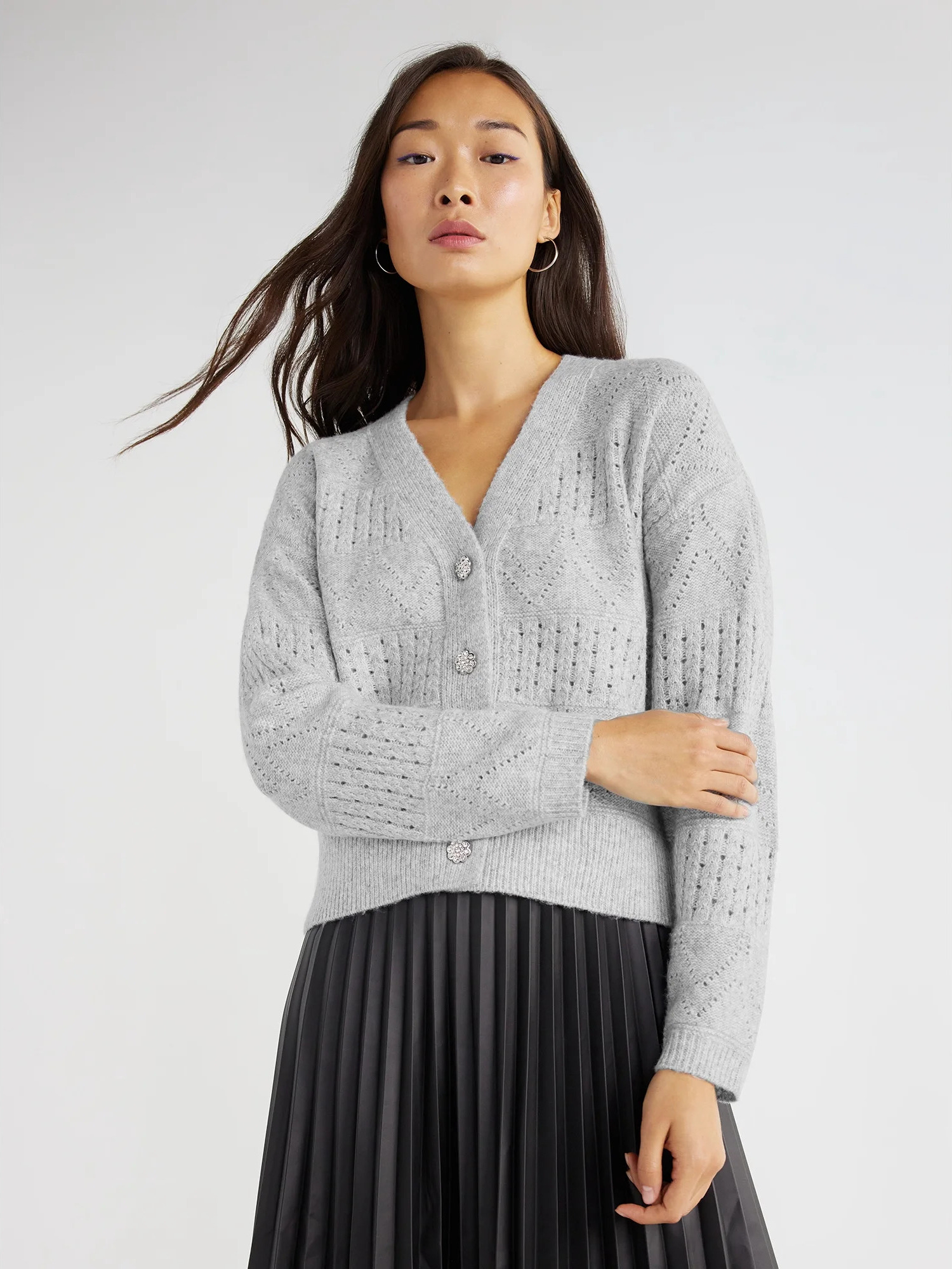 A model wearing the v-neck cardigan in light grey with a black pleated skirt