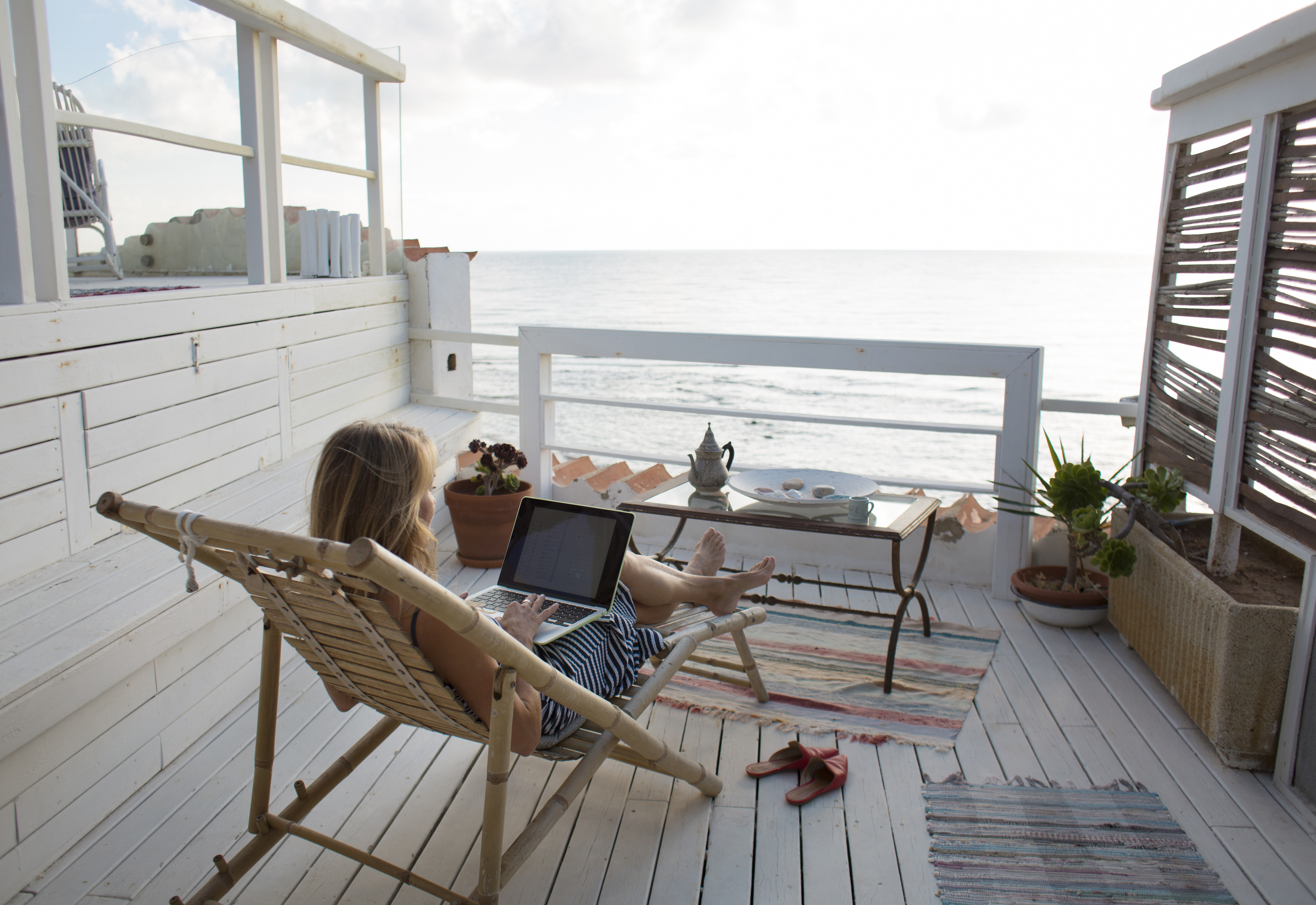 Person sitting outside on a porch overlooking the ocean while working on a laptop