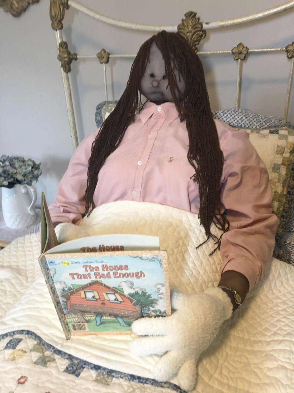 A doll sitting up in bed reading