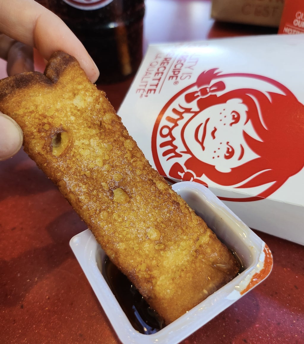 a french toast strip being dipped into a container of maple syrup