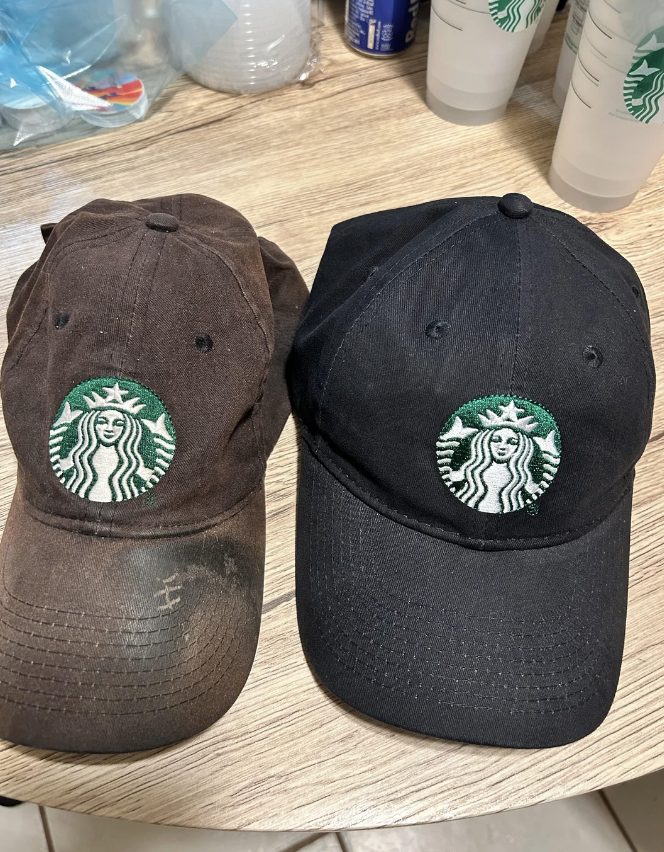 An old barista cap is a dirty dark brown, next to the black new one