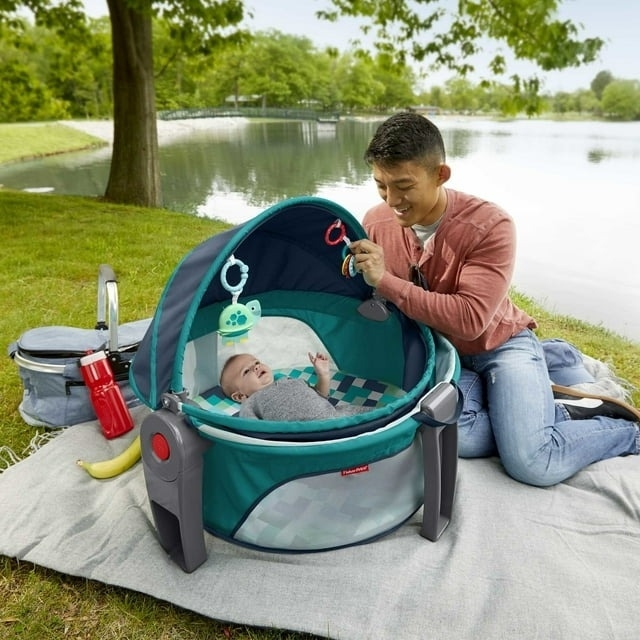 baby laying down in teal portable dome with hanging sensory toys inside