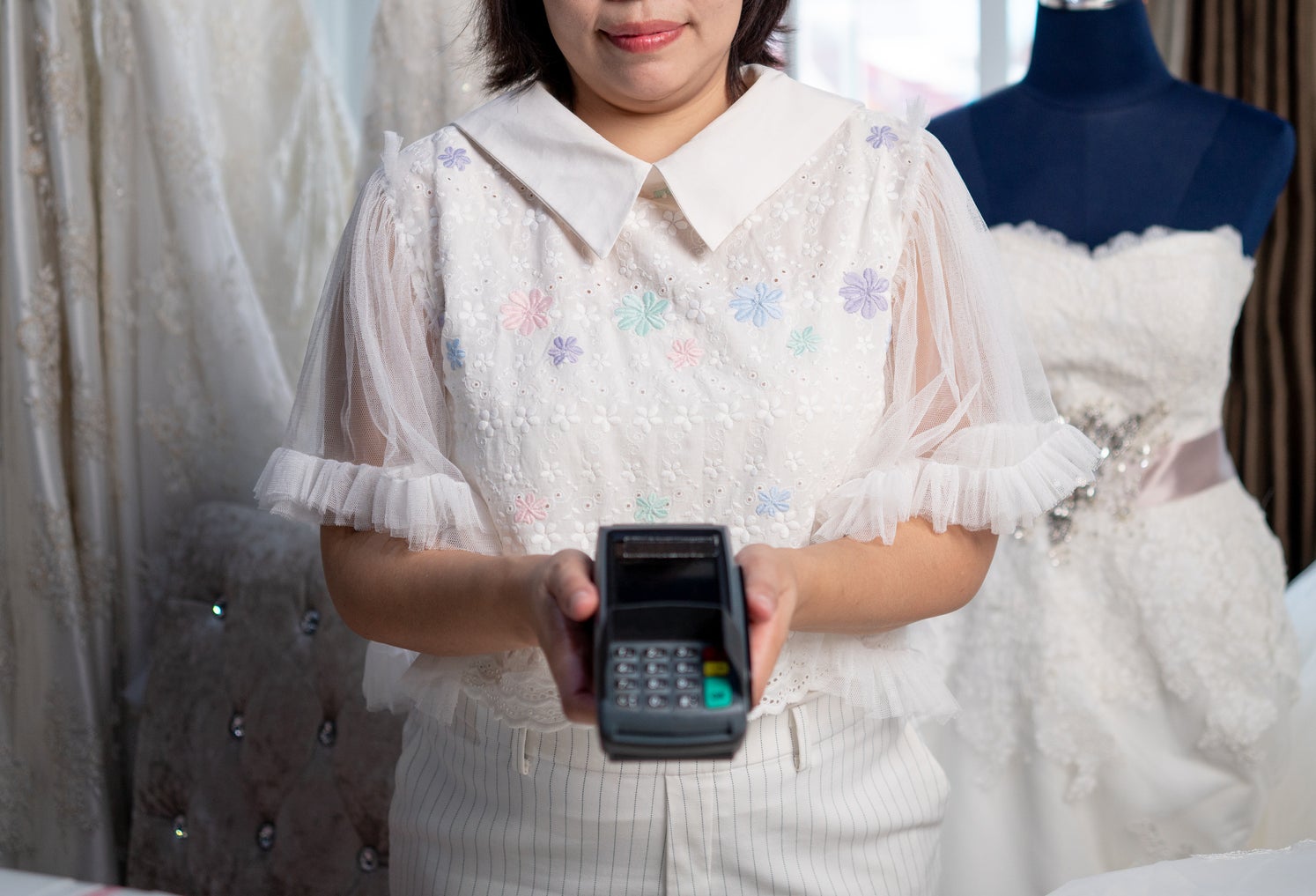 Dress shop accepting payment by credit card machine, woman holds a credit card machine
