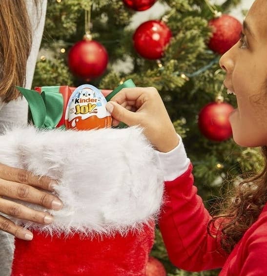 child taking Kinder Joy chocolate treat out of red stocking