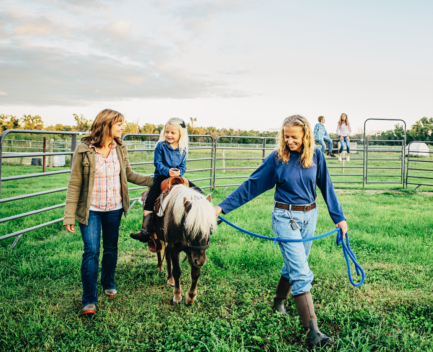 little girl riding a pony with her mom and horse trainer