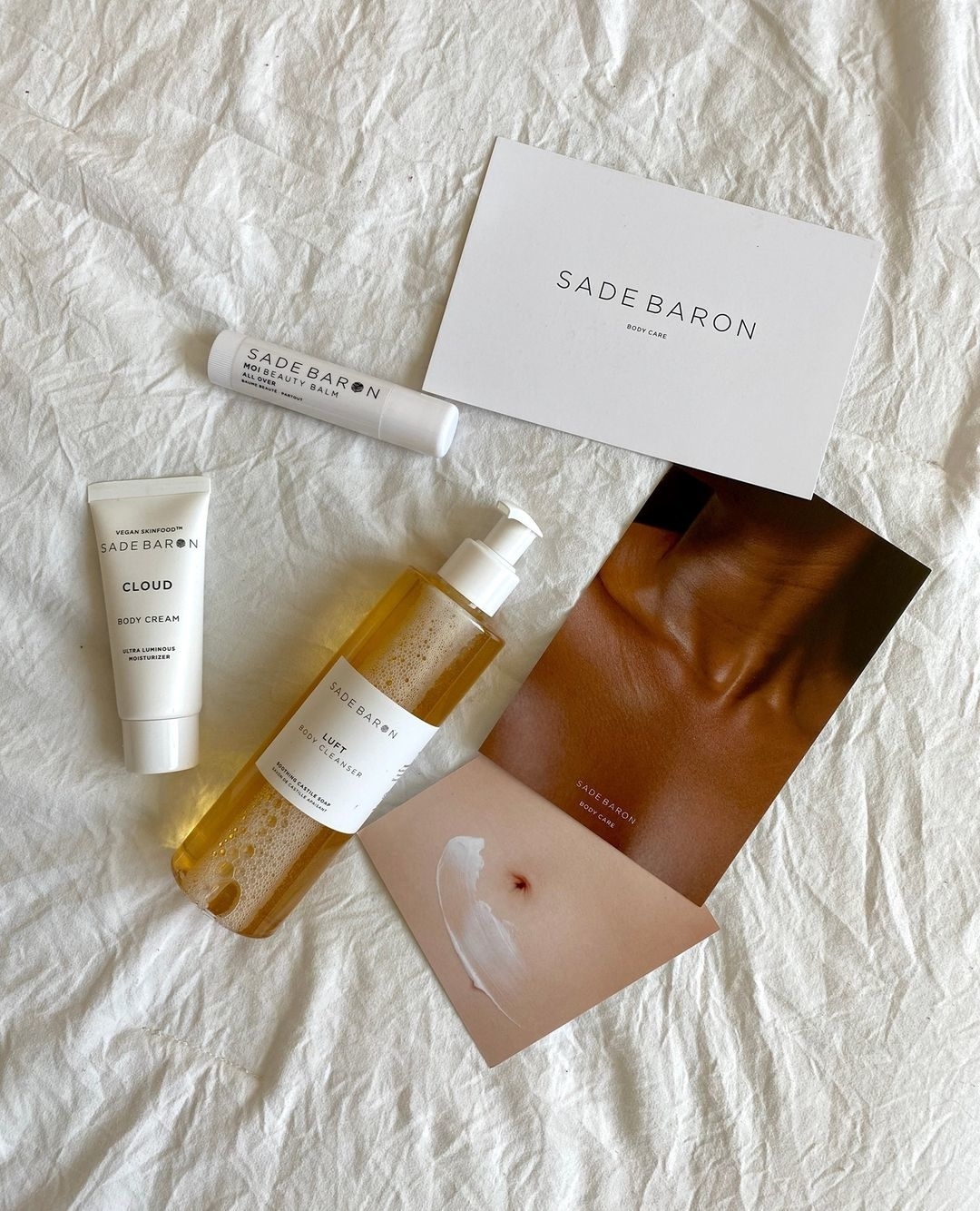 A bottle of body cleanser, body cream, and body balm on a bed