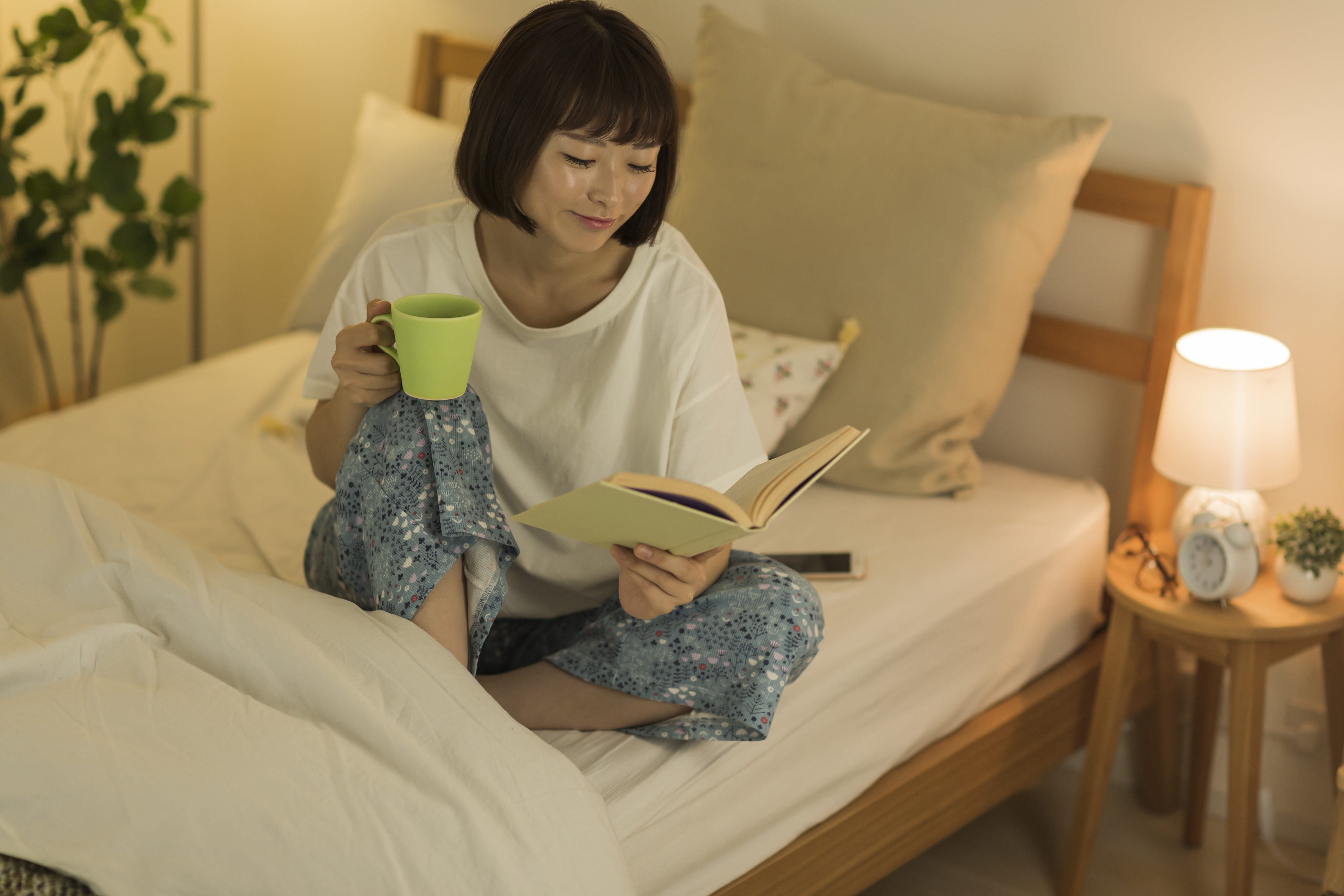 person reading a book in their bed with a cup of tea while relaxed