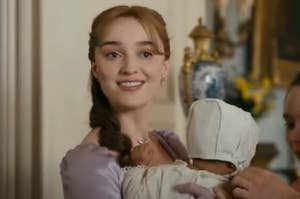 Daphne from Bridgerton smiling while holding her baby