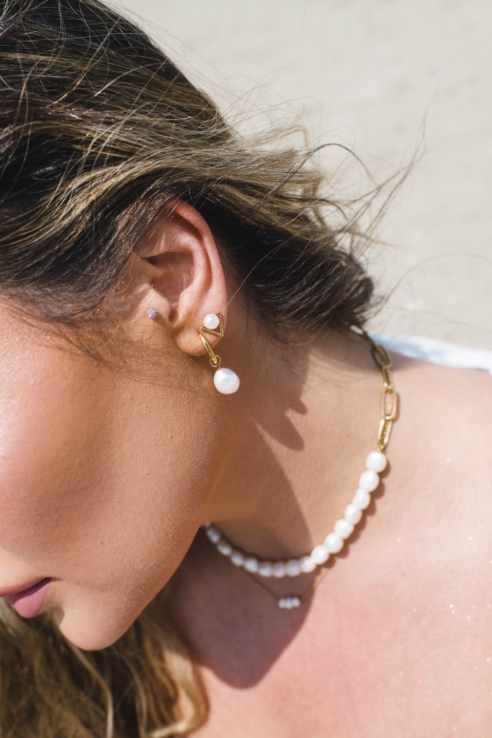 A person wearing  pearl drop earrings and a pearl necklace