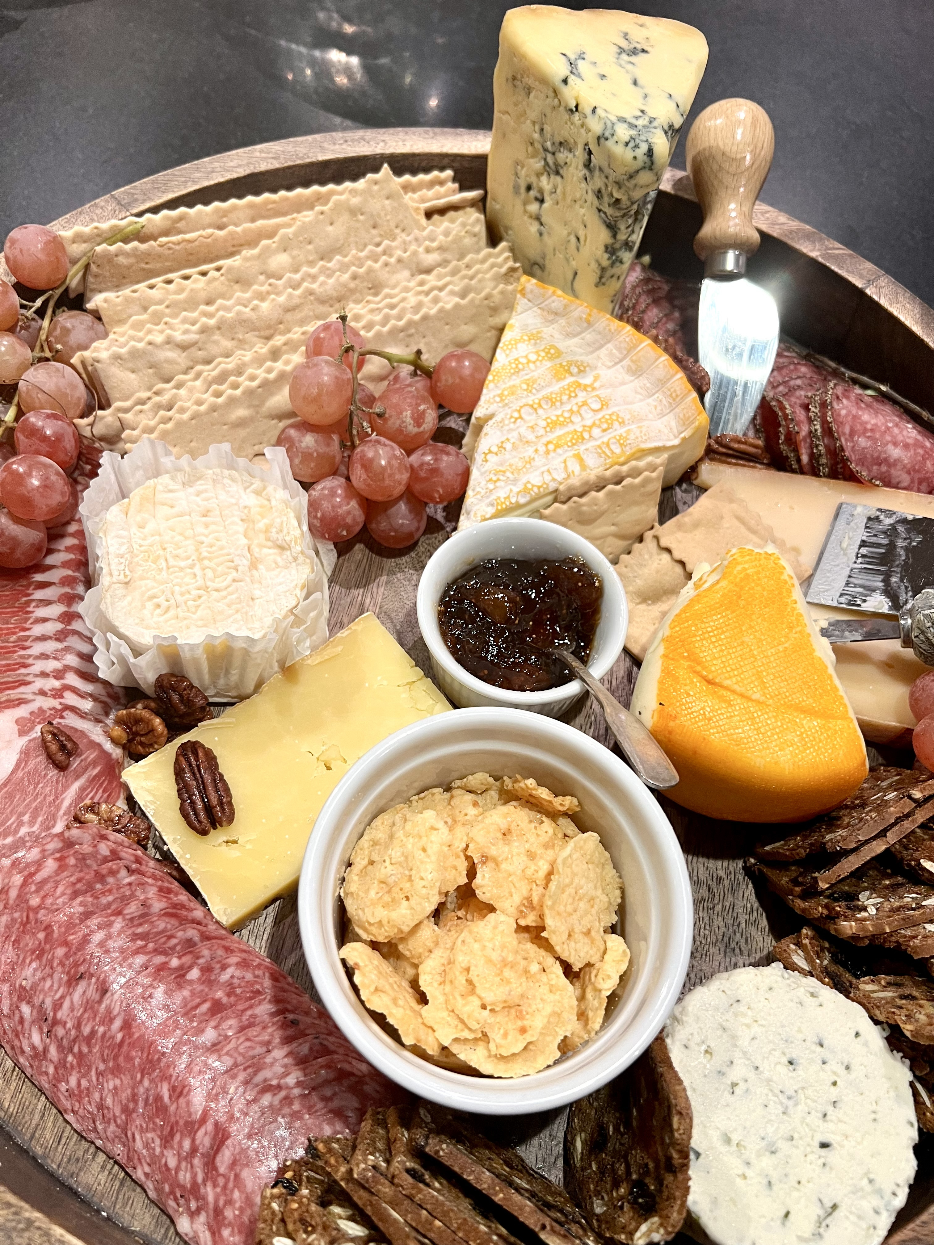 cheese board with various cheeses, crackers, nuts, and fruit atop it